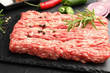 Raw minced meat with rosemary and spices on black table, closeup
