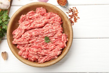 Raw minced meat, parsley and spices on white wooden table, flat lay. Space for text
