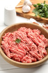 Raw minced meat, parsley and spices on white wooden table, closeup