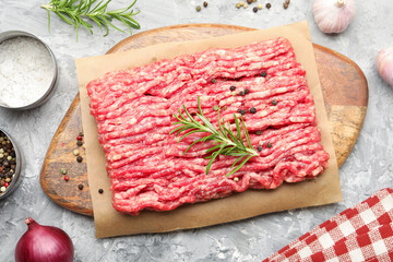 Raw minced meat with rosemary, spices and onion on grey textured table, flat lay