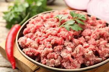 Raw minced meat with parsley and chili pepper on table, closeup