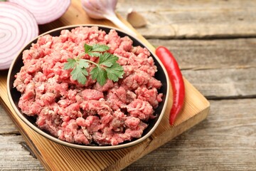 Raw minced meat with parsley, onion and chili pepper on wooden table, closeup. Space for text