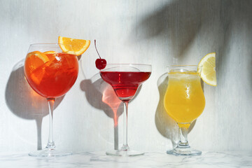 Glasses of tasty cocktails with garnish on white marble table