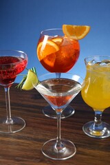 Glasses of tasty cocktails with garnish on wooden table against blue background, closeup