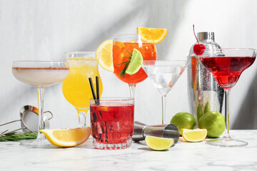 Glasses of tasty cocktails, ingredients, shaker, sieve and jigger on white marble table