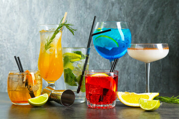 Glasses of tasty cocktails, ingredients and jigger on grey table