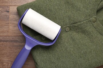 Obraz premium Sticky lint roller and shirt on wooden table, top view