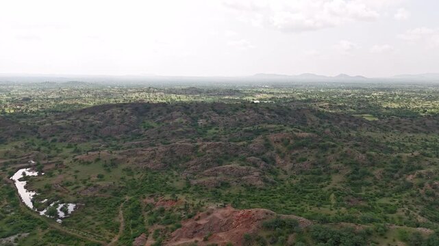 Aerial shot of rocky hills near Masuda, Rajasthan in the Aravalli range, showing native vegetation like Khejri, Ber, Ker, Acacia, and Rohida with moving cloud shadows on a monsoon afternoon
