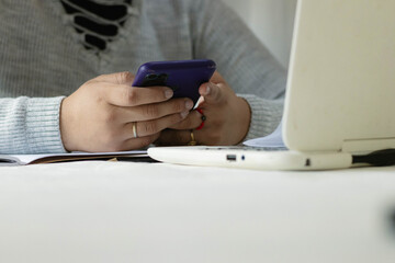 Student procrastinating studying using smartphone instead of laptop