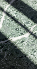 Close-up view of a polished green marble surface with distinct white veining and shadows creating a beautiful abstract pattern