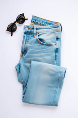 A Stylish Flat Lay of Light Wash Denim Jeans and Tortoiseshell Sunglasses on a Clean White Background, Perfect for Casual Wear or a Summer Outfit