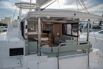 Contemporary catamaran exterior and interior with an open living space featuring light green cushioned seating, dining area, and modern kitchen. Polished chrome supports and large windows enhance the 