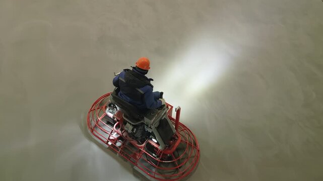 Construction worker operating a ride on power trowel machine. Clip