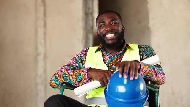 Smiling African construction engineer in a wheelchair holds a blueprint and hard hat, radiating confidence on a building site