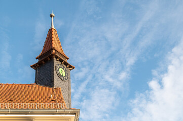 Gedrehter Uhrenturm mit Schieferschindeln und roten Dachziegeln vor blauem Himmel mit Wolken in...