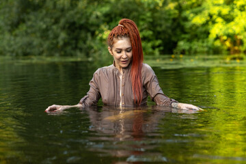 Female figure with red hair is immersed in calm water, surrounded by vibrant greenery, evoking a...