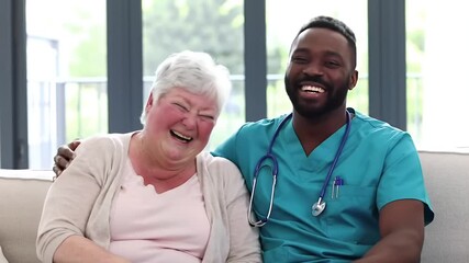 Caring Healthcare Worker Comforts and Shares a Joyful Laugh with an Elderly Woman in a Bright Living Room Setting - Senior Care Concept