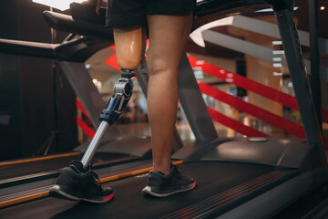 A motivated woman with a prosthetic leg walking on a treadmill in a modern gym, representing...
