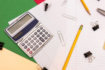 horizontal flat lay of office supplies: calculator, paper clips, pencils, colorful folders, and binder clips
