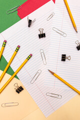 vertical flat lay of office supplies: pencils, paper clips, colorful folders, lined paper, and binder clips
