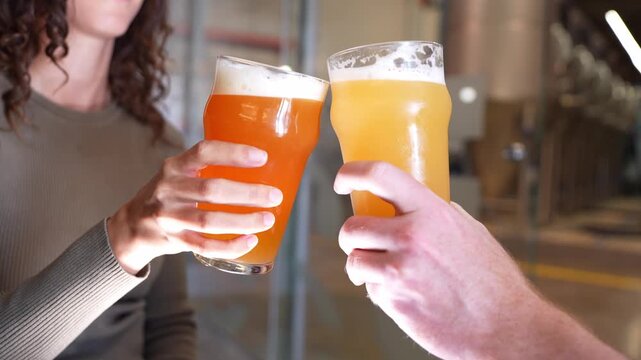 Happy young couple clinking glasses of fresh craft beer at a microbrewery. They are toasting and celebrating with pints of ale and lager