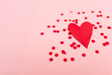 close-up of red and pink confetti and a red cutout heart against a pink background with copy space available