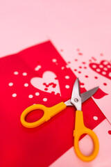 close-up of scissors and red and pink paper cutouts of circles and hearts against red and pink paper; Valentine's day crafting 