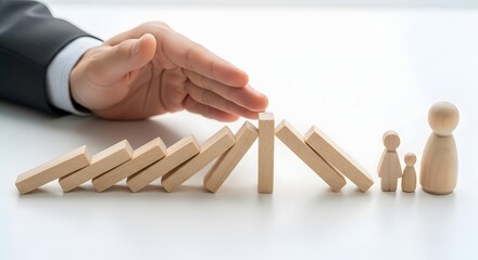 Hand Stopping Domino Effect to Protect Wooden Family Figures.