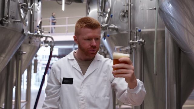 Professional brewmaster in a white lab coat checking the color, clarity, and foam of a freshly poured craft beer in a modern brewery