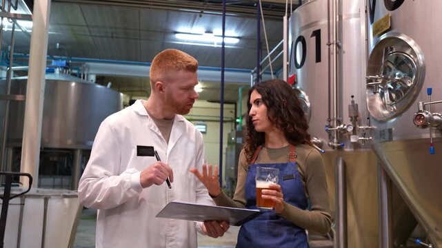 Young female brewmaster tasting craft beer with a male quality control inspector. Colleagues discussing the beverage's flavor and aroma