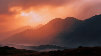 Obraz premium Dramatic mountain landscape at sunset with glowing orange sky and atmospheric mist