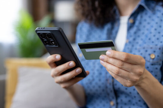 Woman holding black smartphone and green credit card while securely making an online purchase from home, focused on mobile payment, app and private cashless transaction