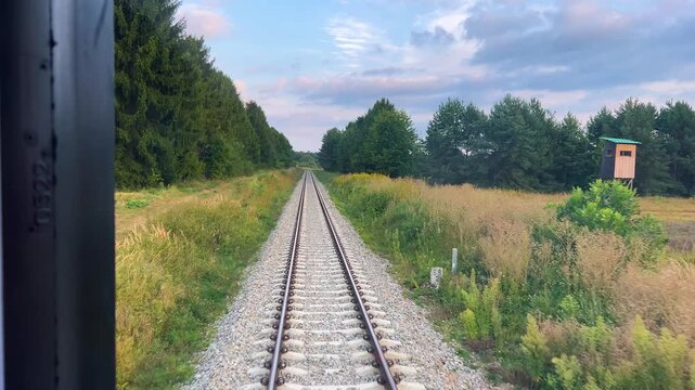 A view from the window of the last carriage of a passing train onto a railway running through a forest in the rays of the setting sun in Poland.