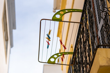Clothespins in various colors hang from a drying rack attached to a wrought iron balcony railing.