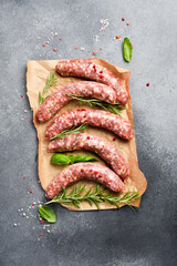 Fresh beef sausages on parchment paper, with spices and rosemary, ready to be grilled. Top view.