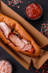A hot dog with sausage, bacon, sauces, and a bun, unhealthy takeaway food. A hot dog with bacon