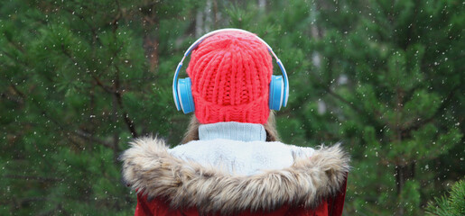Back view woman enjoying listening to music with headphones in winter forest against Christmas tree