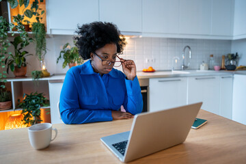 Tired black woman looks at laptop with blurry eyes suffering from computer vision syndrome....
