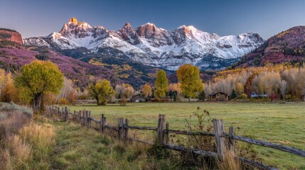 Scenic autumn landscape snow-capped mountains, colorful trees, and a wooden fence