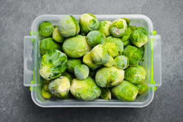 Frozen bunch of Brussels sprouts in a plastic box. Frozen vegetables for the winter. On a gray stone background. Close-up.