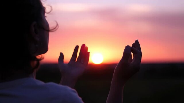 A woman's silhouette holds her hands up to the setting sun. A spiritual moment of prayer and connection with nature. Hope and faith concept