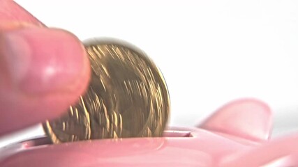 A hand carefully inserts a shiny coin into a pink piggy bank on a bright surface. This everyday activity highlights the simple joys of saving money at home.