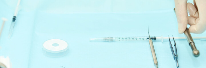 Naklejka premium Surgical tools and medical equipment on blue surface with gloved hand preparing instruments.