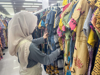 Fototapeta premium A woman admires colorful batik clothing patterns while browsing in a shop