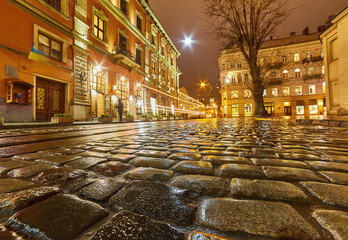 Atmospheric cobblestone street reflecting city lights in an old European city at night.