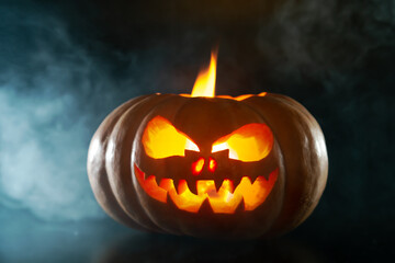 Fototapeta premium Halloween pumpkin with a scary glowing face in smoke.