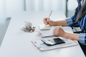 Fototapeta premium Woman Working at Desk: A focused woman diligently works at a desk, the scene showcases her dedication to detail and commitment to tasks at hand. She is seen writing in a notepad