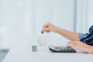 Saving Smart: A person carefully deposits a coin into a piggy bank while using a calculator,...