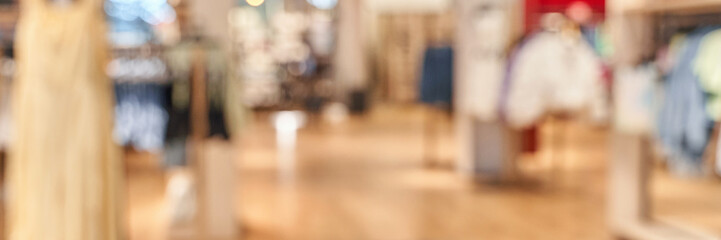 Blurred interior of modern clothing store with racks and displays on wooden floor.