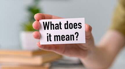 A person is holding a white card that says What Does it Mean. Concept of curiosity and...